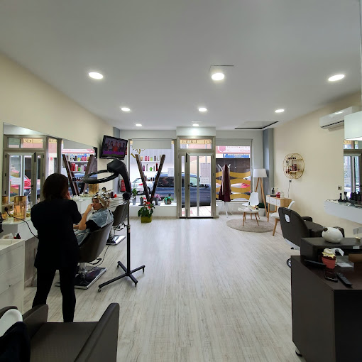 Interior de la peluquería "Laura García" con una vista general del salón, mostrando varias estaciones de trabajo, espejos, y una estilista atendiendo a una clienta.